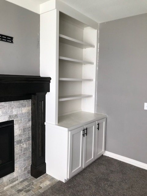 Built-in bookshelf and cabinet beside a stone fireplace by Chapman Custom Craftsman